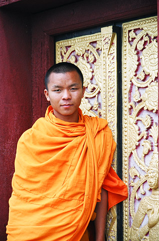 A monk poses in front of the gilded and carved doors of a temple at the summit of the hill site known as Phu Si in Luang Prabang.