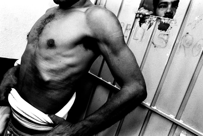 A detained immigrant shows his broken rib while another peeks out from a small window in the detention room. The injured man said police beat and robbed him and left him in an abandoned shed north of Tapachula, Mexico. 
