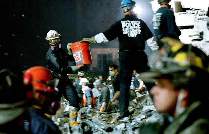 Rescue workers hand buckets of rubble along an assembly line in the night.