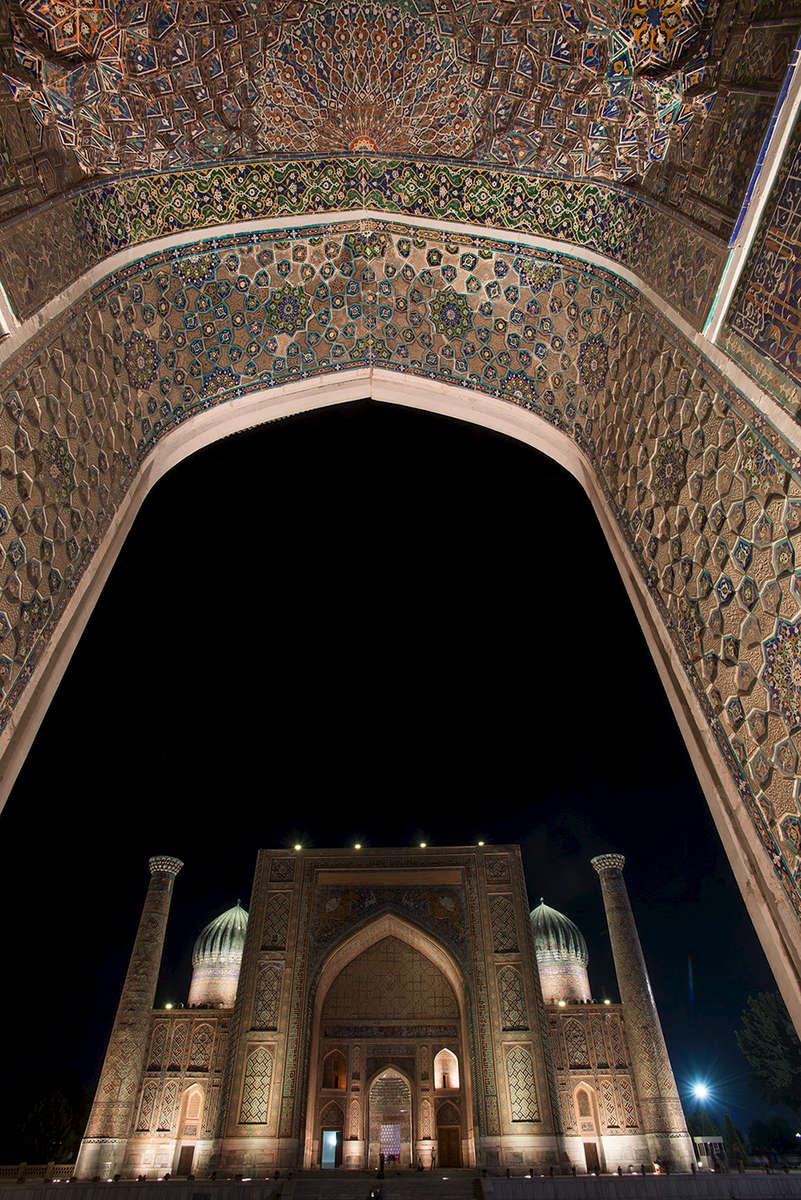 Seen through the entrance portal of the Ulug Beg Madrassah opposite. At night