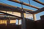 Materials are predominantly local: adobe within a reinforced concrete structural frame, pumice for under-slab insulation, and rough-sawn douglas fir. The roof trusses are made of twin 2x10s flanking a steel strut and tension chord. Spanning increasing distances between straight and curved tie beams, the roof surface takes on a subtle warp.