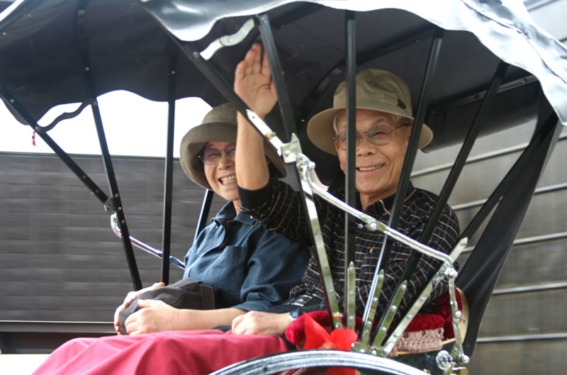  A Japanese couple gives a friendly wave as they pass in a rikshaw in Takayama, Honshu.