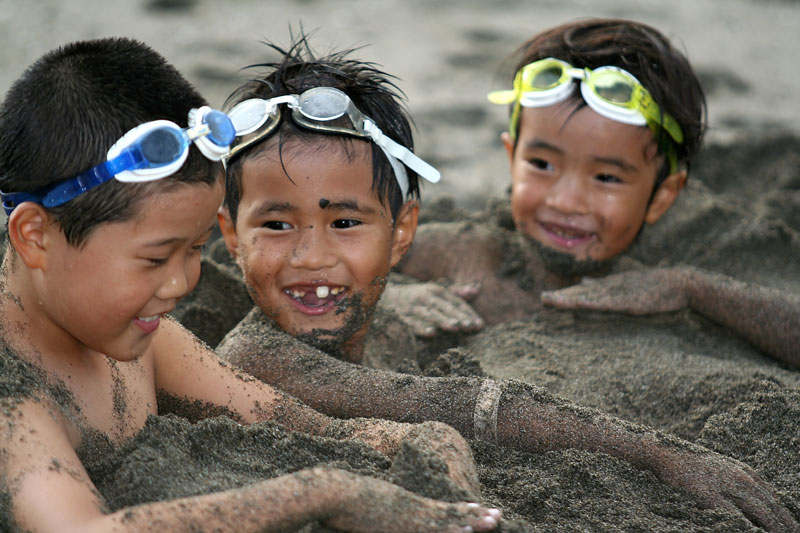 Three boys have fun on the beach after being burried in the sand.