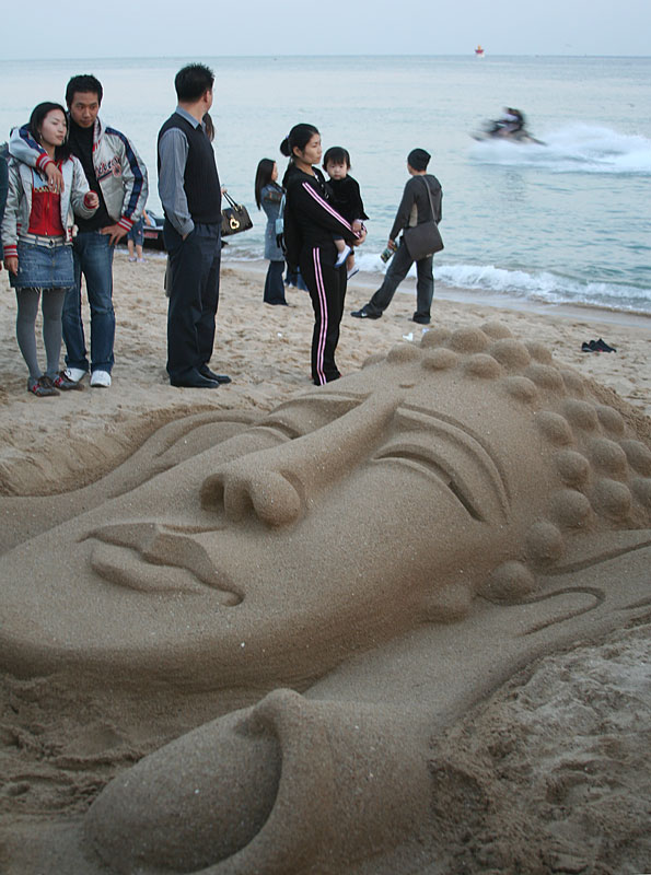 People gather around a sand sculpture on Haeundae Beach as a Sea-doo  races past in Busan, South Korea.