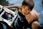 A young boy digs through sewage-filled water, searching for anything salvagable, on the Pasig River in the Paco Market neighborhood of Manila, one of the city's worst slums.  The neighborhood was hit particularly hard by the slew of typhoons.© Habitat for Humanity International/Ezra Millstein