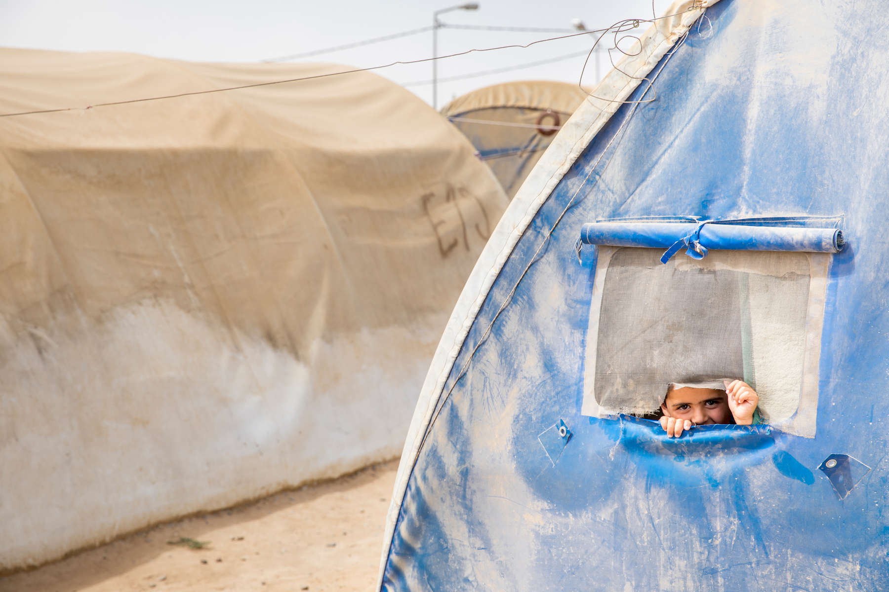 A boy looks out the window of his family's tent at the Jeddah IDP camp. Families fleeing the violence in Mosul are often unable to bring anything with them. In displacement camps, Mercy Corps is delivering essential supplies to help people survive. New arrival kits include: cooking pot and pan, plates, glasses, silverware, serving spoon, stainless steel kitchen knife, 6 light weight blankets, 1 rope, 1 tarp and 2 jerry cans. To provide one family with these household essentials costs approximately $70 USD / 60 Euro / 54 GBP.