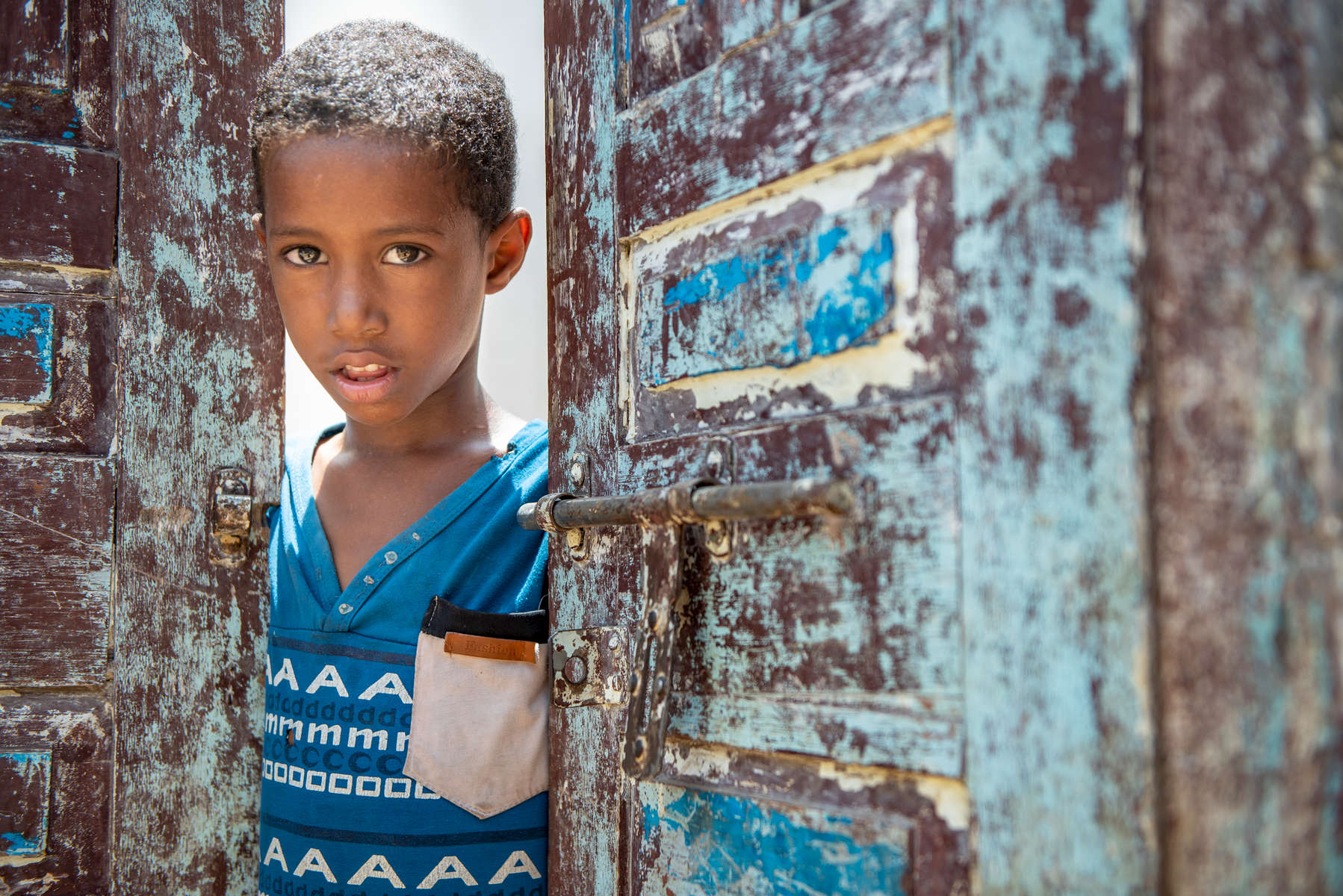 Ali, 9, peeks through the doorway of his family's home. His father Wassim used to work as a day laborer, trying to find work wherever he could to support his four children, but jobs are scarce in war-torn Yemen. He would travel far and still not be guaranteed to find enough work to support his family’s basic needs. Wassim was hired by a Mercy Corps cash-for-work project, and helped build an irrigation channel. He used the money to buy a cow and some sheep, and opened a vegetable stand, so he could begin to earn a regular income.