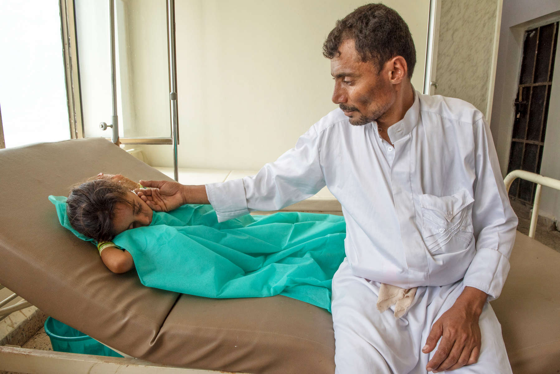 Abdullah and his 7-year-old daughter Nehan in a cholera isolation unit, where Nehan has just begun receiving treatment. Mercy Corps is providing cholera clinics with beds, IV fluids and water to help them meet the increasing needs of patients like her.