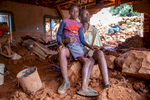 Anthony Machingauta, 52, is a schoolteacher. His son Leonard, 15, sits on his lap in the middle of their home. On March 16th, rains from Cyclone Idai unleashed mudslides from the hills surrounding Ngangu, which crushed the front wall of their house and exited out a side wall, leaving 4 feet of mud and unmovable boulders throughout their home. Anthony and his three sons all survived, but he is concerned about how he will be able to afford to feed them and pay their school fees.