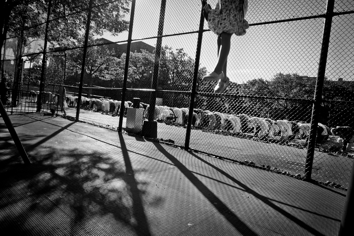 9/24/15 NY Neighborhood profiles series.  Jackson Heights Queens. Travers Park, morning Eid prayer. A child plays in a swing nearby. © 2015 Yunghi Kim/Contact Press Images.