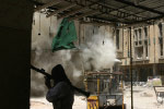 A Mehdi Militia fighter takes cover behind a brick column as U.S. shells hit a nearby building.