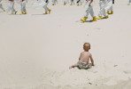 A cleanup crew wearing protective suits walks past a small child playing in the sand on a beach on Dauphin Island, Alabama, on Wednesday, May 12, 2010, as they comb the beach for traces of oil from the Deepwater Horizon oil spill.   The spill released millions of barrels into the Gulf of Mexico over a three month period.  Its long-term impact on the region is still unclear.  