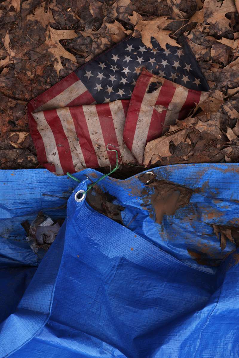 A flag soaked in mud sits attached to a tent. The homeless encampment on the edge of uptown Charlotte, which sprung up as shelters limited capacity due to the pandemic, is being now being evacuated due to a county public health order. (Travis Dove for Axios Charlotte)