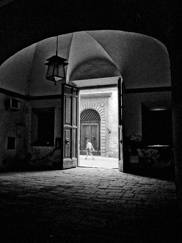 A woman walking down a narrow quiet street is framed in an ancient doorway.