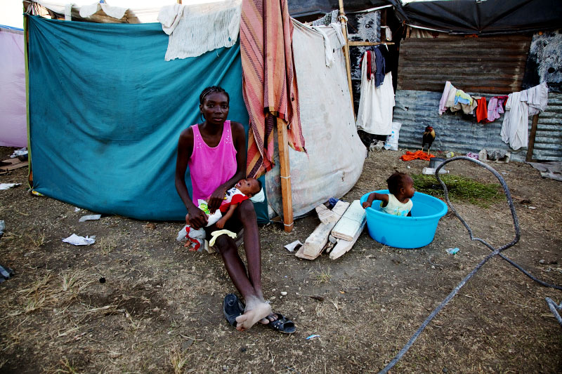 At Pont-Rouge refugee camp, 31 year old Haitian earthquake survivor Mona Lamour holds her 2 month old baby Naida in front of  her tent, as her another child stays nearby.