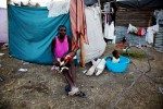 At Pont-Rouge refugee camp, 31 year old Haitian earthquake survivor Mona Lamour holds her 2 month old baby Naida in front of  her tent, as her another child stays nearby.