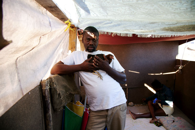 At Pont-Rouge refugee camp, 38 year old Haitian earthquake survivor Jean Enel Montinor holds a hen, as his 29 year old wife Erline stays nearby in his tent where 8 family members live together. The hen is not for the eating. It has a name of {quote}Lina,{quote} and treated as a family member, as Jean Enel lost his mother and father due to the quake.