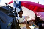 At Pont-Rouge refugee camp, 9 year old Haitian earthquake survivor Sherley Hogsylin holds a doll, as her relative stays nearby in her tent where 6 family members live together. 