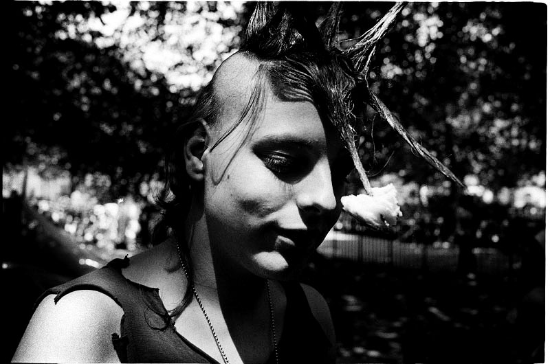 A female squatter in the park makes fun or fools herself, penetrating a piece of bagel into her punk hair. July 1989.