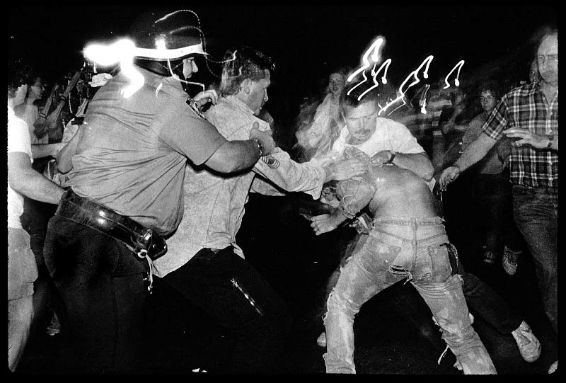 Just outside Tompkins Sq Park, a riot geared policeman and three undercover officers are about violently to arrest a homeless-rights activist who was hitting a trash can as drum. Many human rights advocates had criticized NYPD for the use of excessive force as it confronted Tompkins protesters. New York, July 1989.