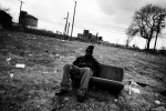 A homeless man sits on a sofa, that was a part of a car, in an abandoned, burned out empty lot in Detroit Downtown. March 2009.
