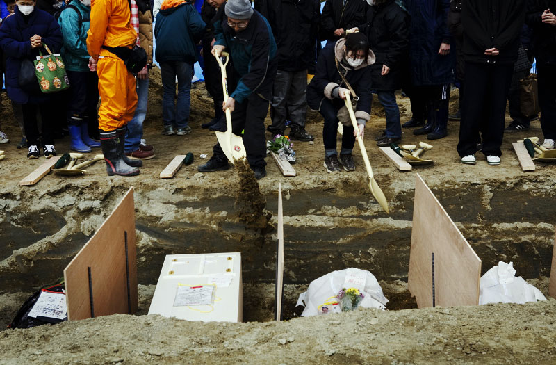 Family members of victims of the monster tsunami put sands onto coffins during the mass burial ceremony in Oshio district in Higashi-Matsushima, Miyagi.