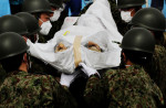 Japanese soldiers carry a victim of the monster tsunami into a mass burial site in Oshio district in Higashi-Matsushima, Miyagi.