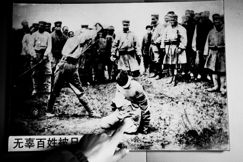 A volunteer Chinese guide points out her finger onto a photograph, saying that A Japanese soldier is executing an innocent farmer during the Japanese occupation of Manchuria. It hangs at a wall of the rebuilt Shuishiying where Japan and Russian signed a ceasefire agreement.