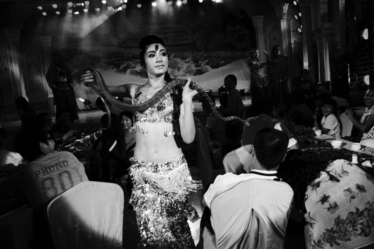 A Uighur woman performs a belly dance with a live snake in front of Han Chinese customers at a club in Urumqi. Although the dress is un-Islamic, many Uighur women, Muslims, like her, take such a performing job to make ends meet.