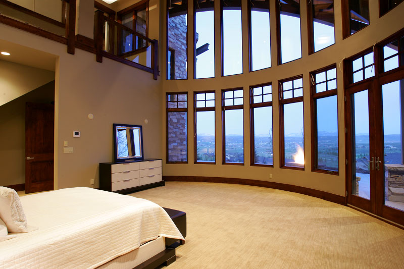 Interior master bedroom with carpeted floor and high glass curved windows with view of upper level deck
