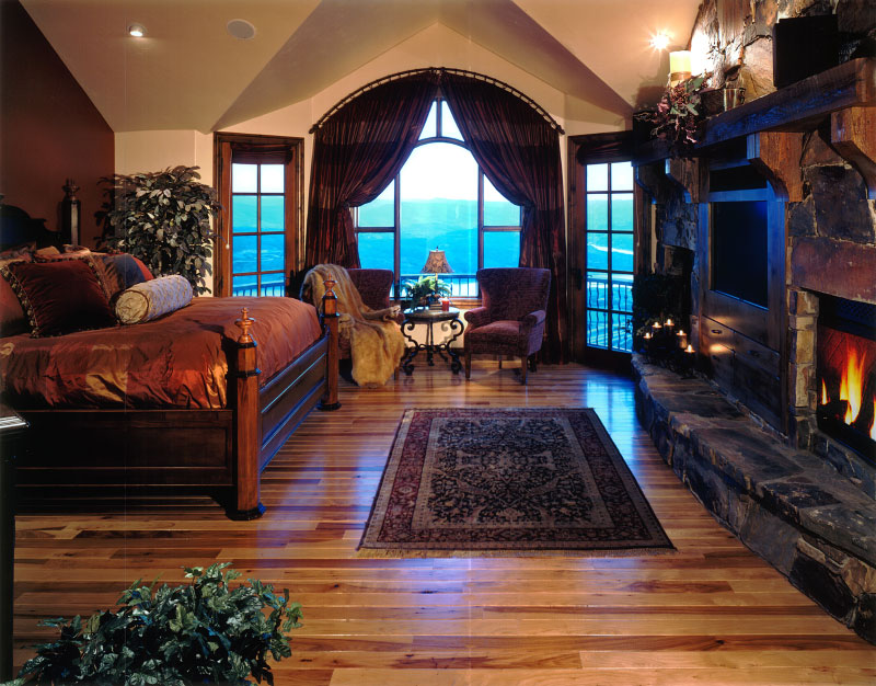 Interior upper level bedroom with wooden flooring, firepit, and seating area by windows 