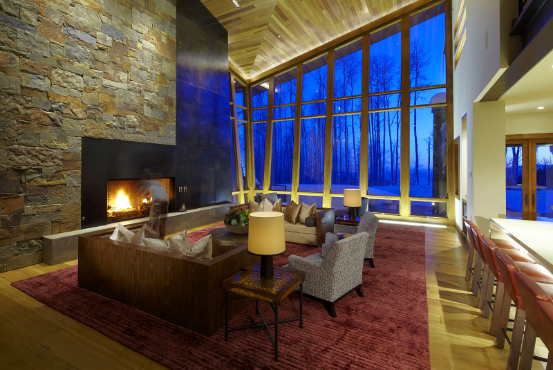 Exterior living room with large stone veneer fireplace and large glass windows with wood framing 