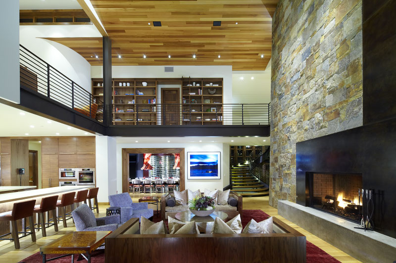 Interior family living room with large fireplace, view of upper level deck, kitchen countertops and family dining table 