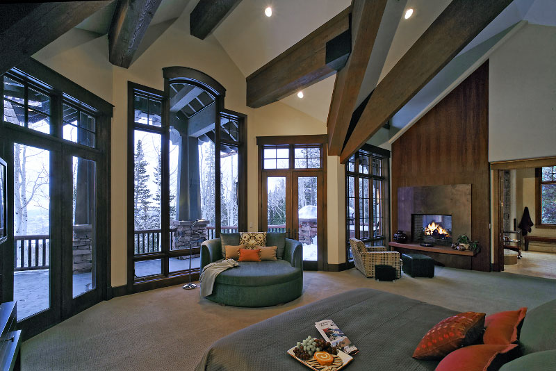 Interior upper level bedroom with fireplace and high glass windows leading to upper level deck