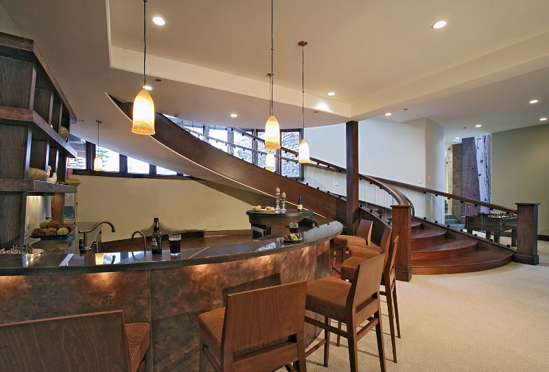 Interior lower level copper bar with marble countertops, carpeted floors and bottom of wooden stairwell
