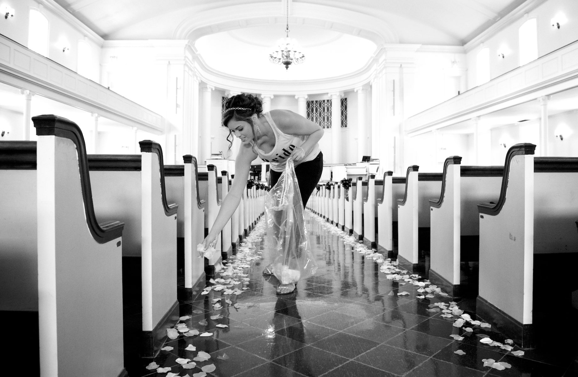 Adria sprinkles rose petals down the center aisle of MacMurray College's Annie Merner Chapel as she prepares for her wedding ceremony. Wedding photography by Steve & Tiffany Warmowski.