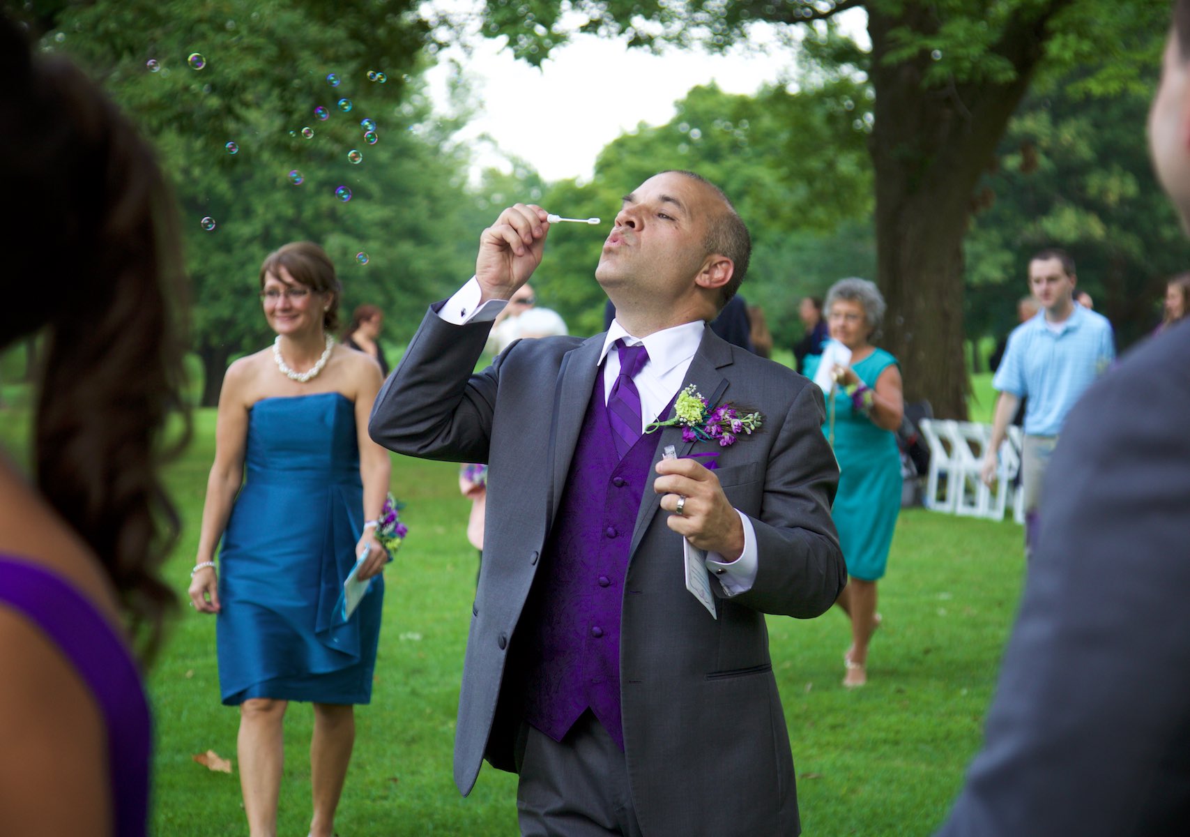 Nick's father blows bubbles after the outdoor wedding ceremony at the Jacksonville Illinois Country Club. Wedding photography by Steve & Tiffany Warmowski.