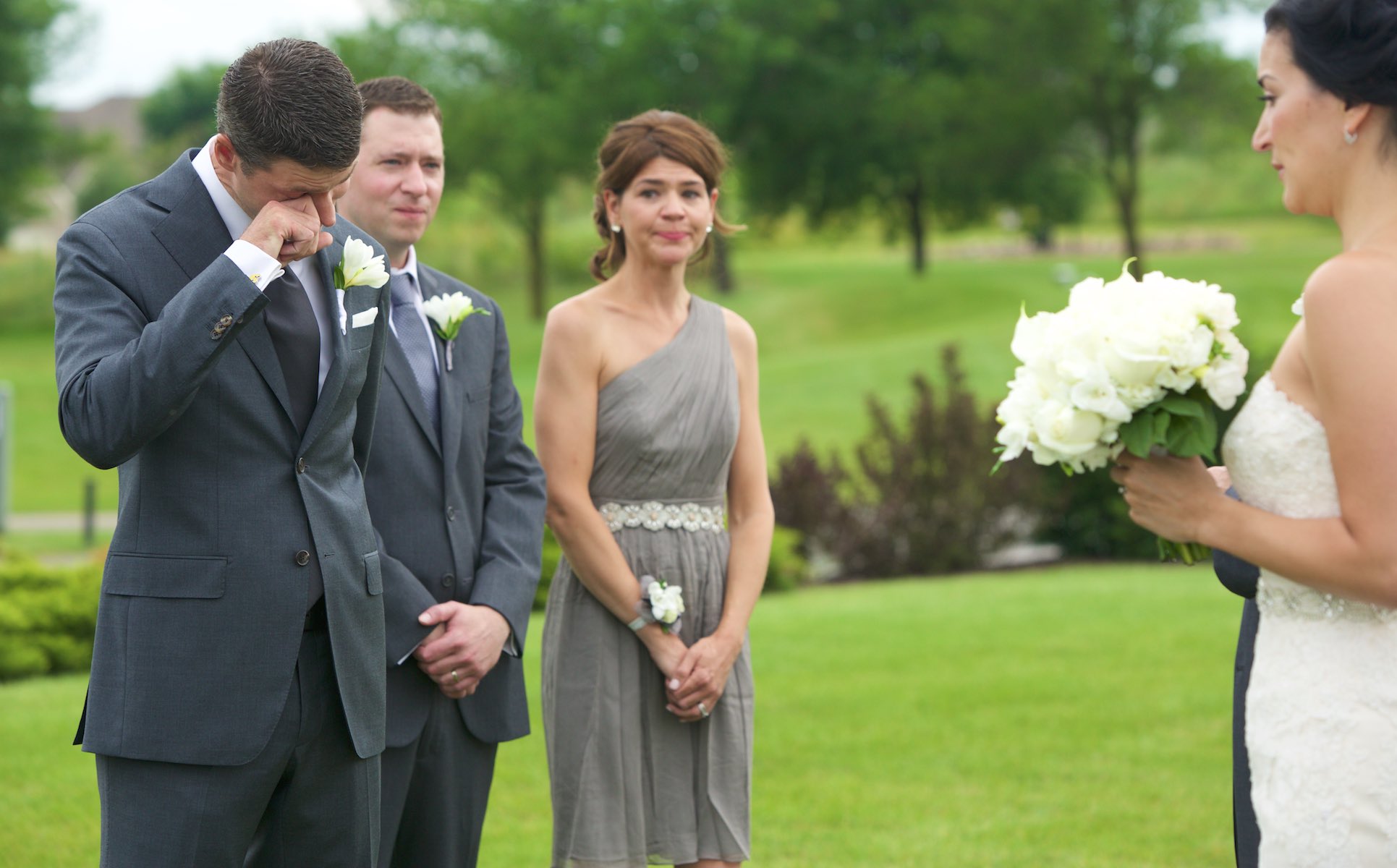 Daniel reacts as Emi comes down the aisle, wedding ceremony at Geneva National Golf Club in Lake Geneva, Wisconsin. Wedding photography by Steve & Tiffany Warmowski.