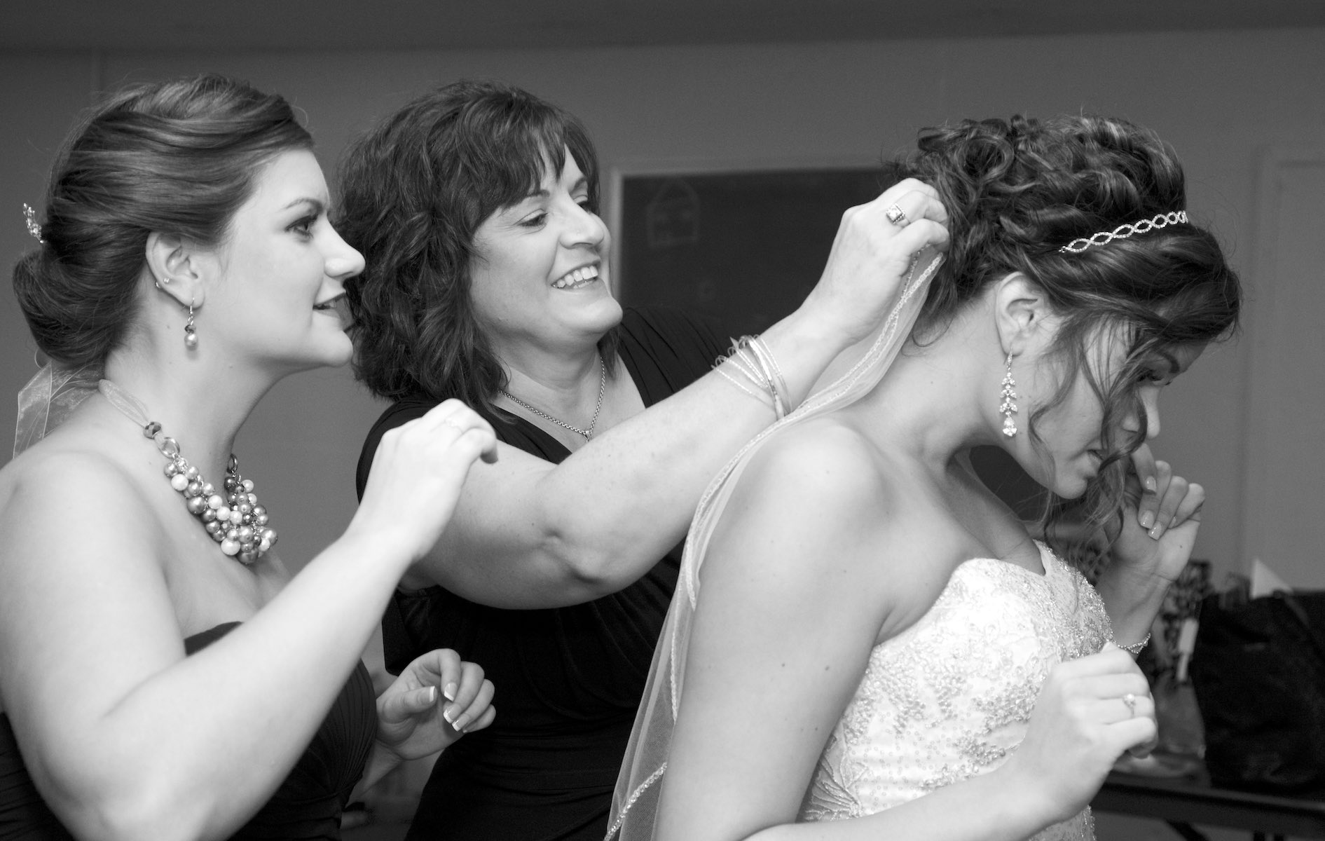 Adria gets help from her mother and sister as she she gets ready in the basement bridal room at Annie Merner Chapel,  MacMurray College, Jacksonville, Illinois. Wedding photography by Steve & Tiffany Warmowski.