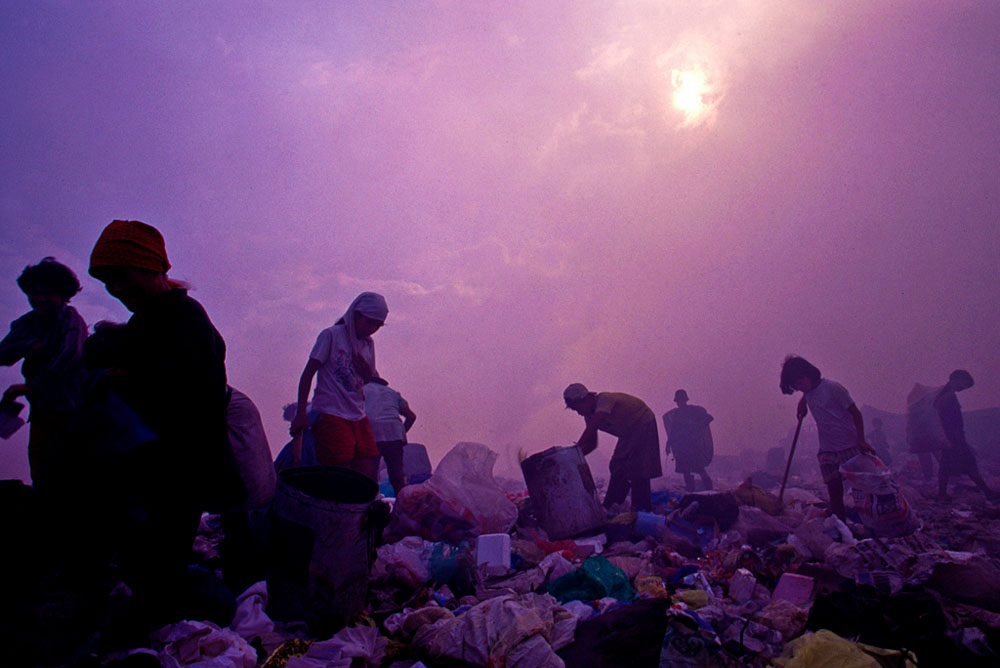 Working in hazy and smokey skies workers look through trash for recyclable materials. Much of the trash is burned in the same areas where people are working putting out toxic smoke.