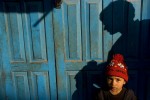 A young boy stands against a door on a street in Kathmandu, Nepal.