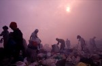 Working in hazy and smokey skies workers look through trash for recyclable materials. Much of the trash is burned in the same areas where people are working putting out toxic smoke.