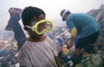 A young boy uses a swim mask to protect his eyes from the burning smoke while working at the Payatas. Much of the trash is burned in the same areas where people are working putting out toxic smoke.