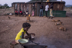 May 6, 2018: KANENGUERERE, ANGOLA - Eleven year-old Regina helps to prepare dinner for her family in front of their home in Kanenguerere Village. The family moved into Kanenguerere village recently so that the children could go to school, and they have a small plot of land by the river where they grow a few vegetables.  The girls, especially, love the HALO deminers and want them to stay in the village forever. The HALO team has Sundays off, so the day is spent going to church, relaxing, and getting caught up on work.  These deminers are working under extremely difficult circumstances in Kanenguerere.  Not only is extremely hot - with snakes and scorpions common - but much of the mined area is on the side of an extremely steep hill, making every step dangerous. The area was mined during the civil war by government forces to protect the nearby railway line that can be seen in the background, as well as various troop positions. It is currently used by roughly 170 people including village residents and nomadic herders - many of whom are young children - who pass through uncleared land every day. 