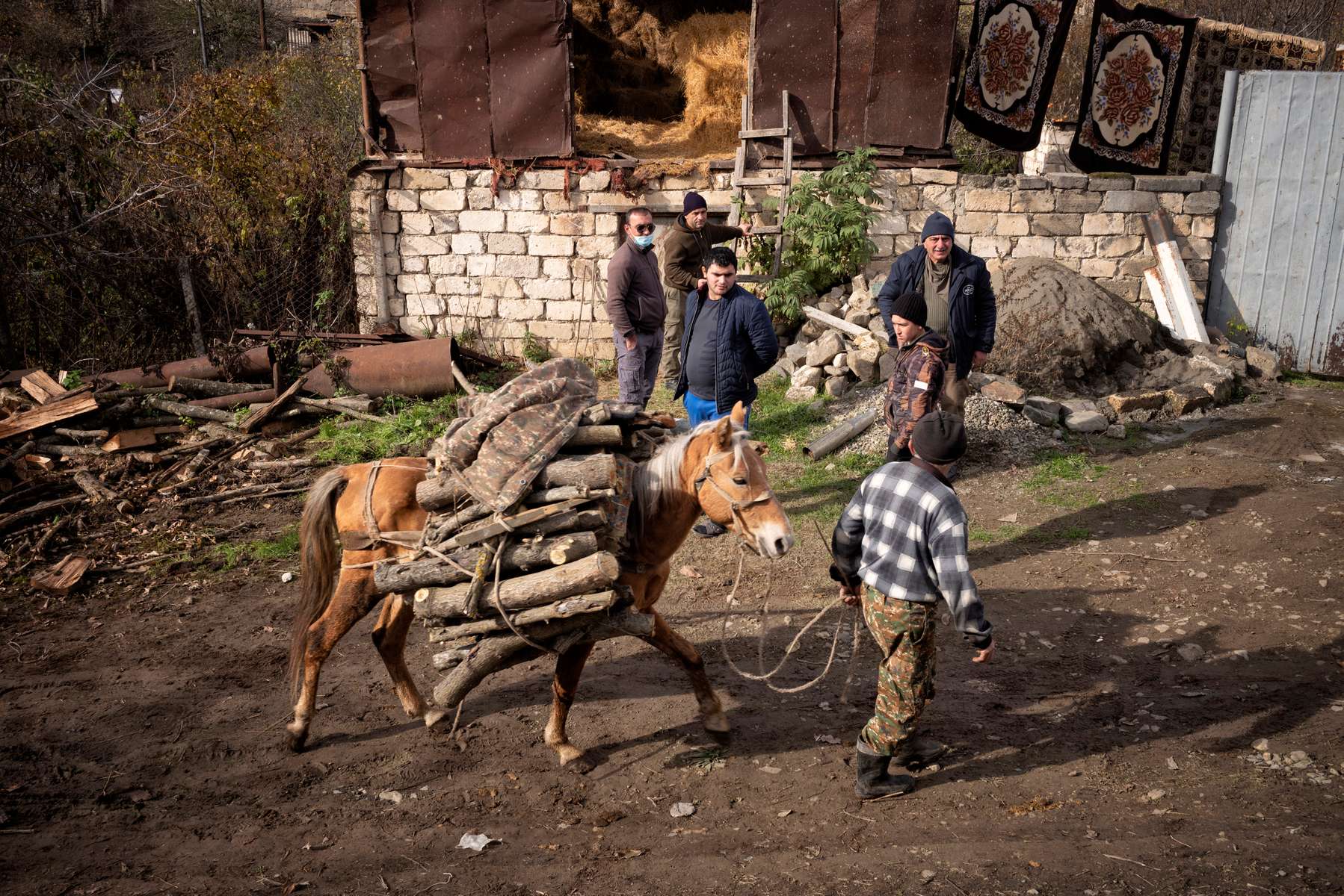 A man leading a donkey cart through Aygestan village, passes the explosive ordnance disposal team from the HALO Trust, who are beginning the laborious process of removing the dangerous explosives, including warheads, rockets, and fuses, that were strewn across the village, when a nearby ammunition storehouse was hit early on in the war. 