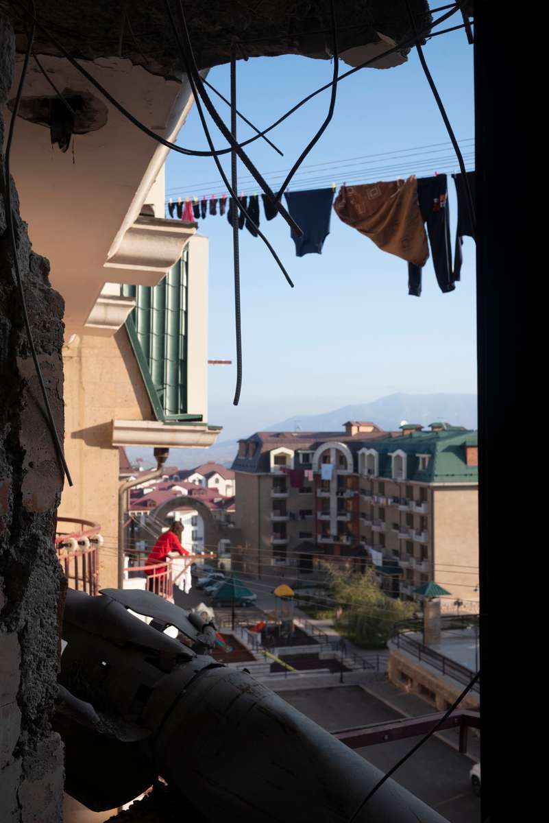 A woman in red hangs laundry out to dry in her home in Stepanakert.  Even nice apartment blocks like this one, with its playground and family-friendly apartment units, were scarred by the war, and her neighbor still has a Smerch rocket embedded in his bedroom wall. 