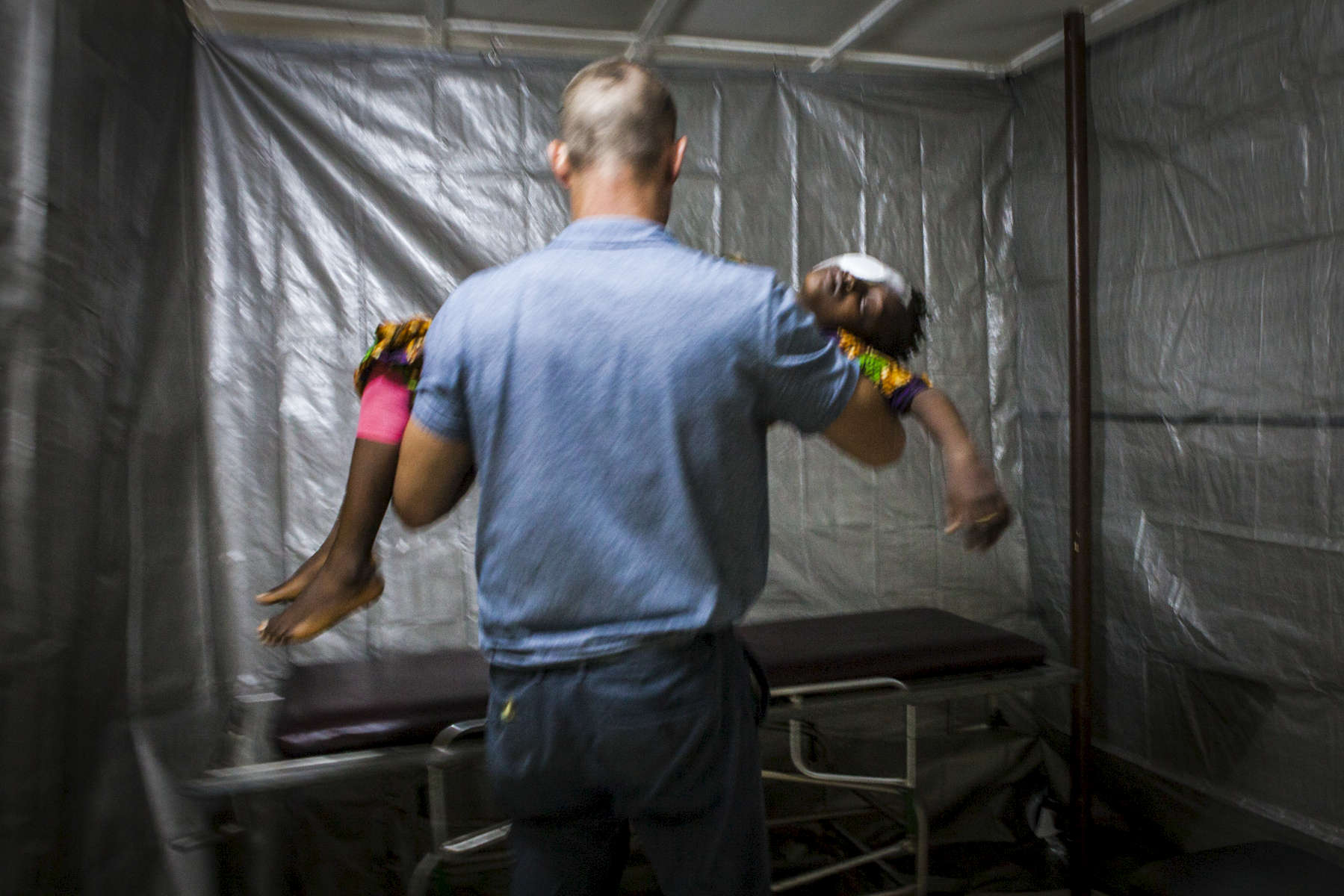 Dr. Ian Crozier carries a sedated Aminata Conteh after her cataract surgery in a makeshift operating room at the Kissy United Methodist Church Eye Hospital in Freetown, Sierra Leone. Dr. Ian Crozier became ill while volunteering for the World Health Organization during the Ebola outbreak in West Africa. Months after recovering from the virus in the United States, Dr. Crozier began to experience intense pain and fading eye sight. After testing doctors found that the Ebola virus still remained in his eye despite testing negative in his blood. 