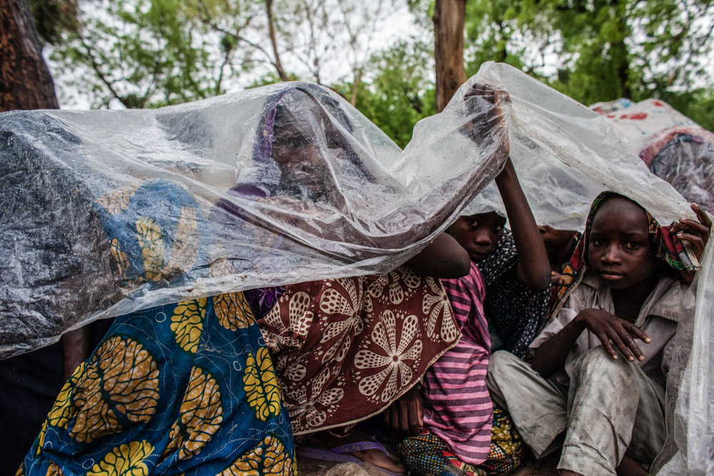 Displaced women and children take cover under a tarp from the rain in Maiduguri, Nigeria.