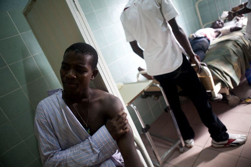A young man who was injured lies on a gurney as a nurse attends to another injured man in a clinic in Treichville, a suburb of Abidjan, Ivory Coast on Tuesday, March 8, 2011. Women marched through the streets of Abidjan today mourning the deaths of seven women killed last week by security forces loyal to Laurent Gbagbo. In Treichville, after finishing prayers (both Christian and Muslim) the marching women encountered the {quote}Compagnies Republicaines de Securité{quote} (CRS), special riot police loyal to Laurent Gbagbo. Its reported that the neighborhood youth guard stood in a line between the women and the CRS to protect the women when the CRS opened fire. At least four were killed including one woman and unknown number were injured.