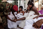 A member of the presidential guard helps his younger sister with her shoe, as other brides look on, just before her wedding outside of a hair salon in Conakry, Guinea